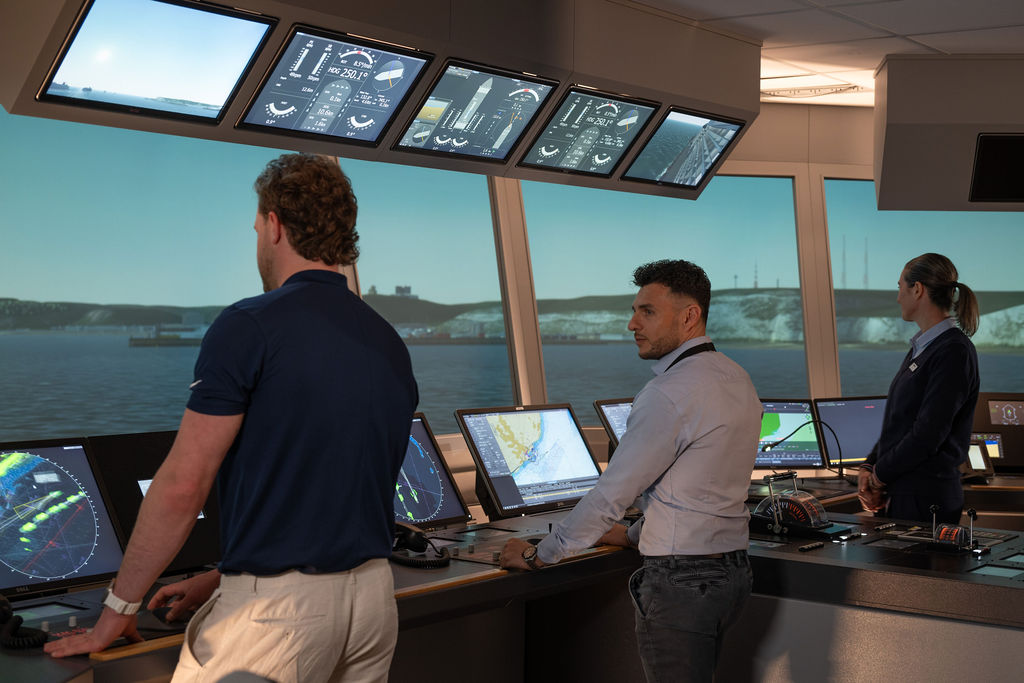Trainees at a ship's bridge simulator console with a panoramic ocean view